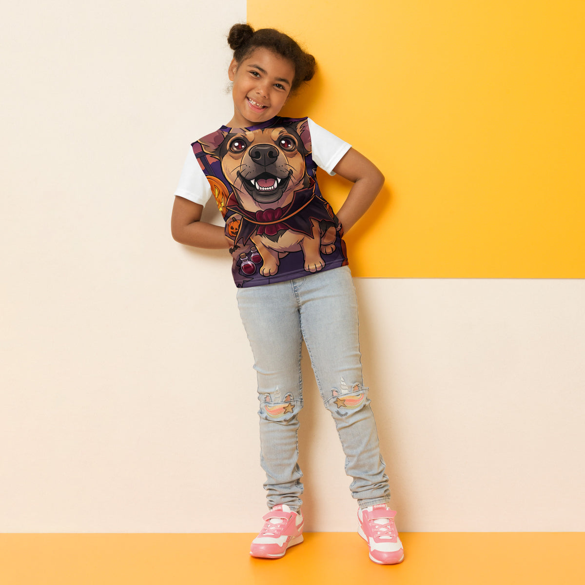 Smiling young girl with hair buns, hand on hip, in a 'spooky pup' all-over print kids t-shirt, vampire dog, cozy bluesky