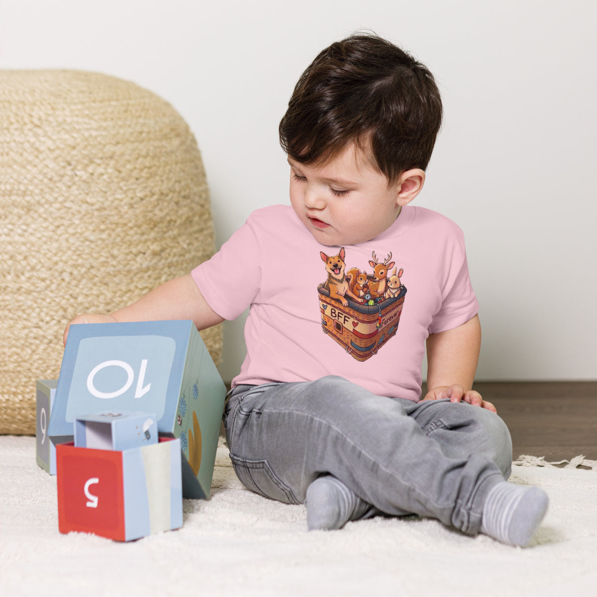 Seated toddler boy wearing a pink 'bff' toddler t-shirt, dog with its squirrel, deer and bunny friends, cozy bluesky