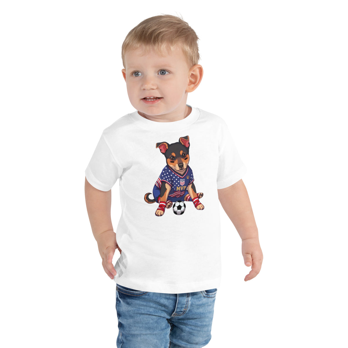 Toddler boy in jeans wearing a white 'soccer MVP' toddler t-shirt, dog in a soccer jersey with a soccer ball, cozy bluesky